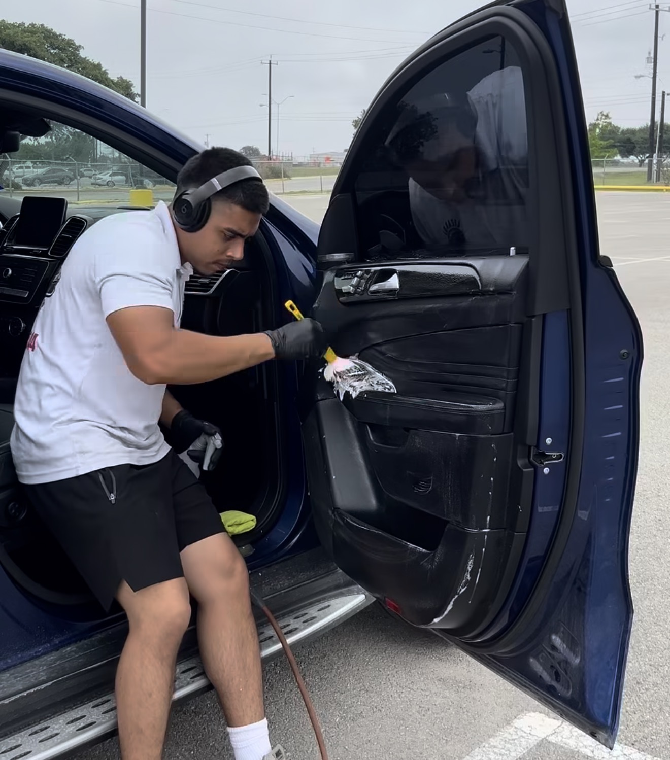 David, owner of Lizardi Mobile Detailing, scrubbing a vehicle door panel on-site in San Antonio